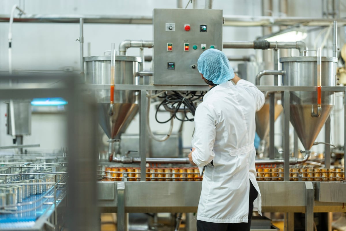 Worker overseeing automated food packaging machinery on a modern manufacturing line